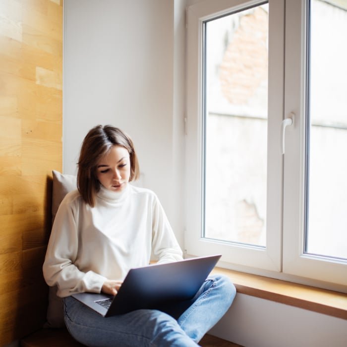 Une femme assise sur un rebord de fenêtre en PVC, utilisant un ordinateur portable